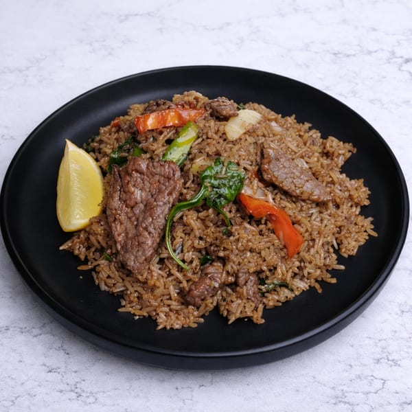Linjee Thai's beef fried rice with red peppers, green beans, and a lemon wedge on a black plate.